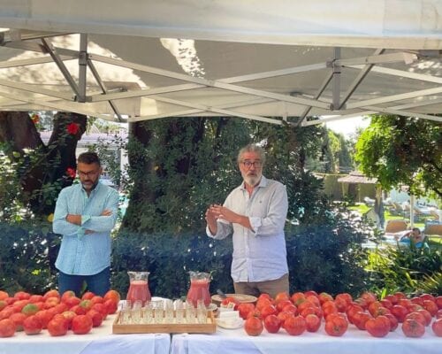 Two men promoting the wellness benefits of a table full of tomatoes.