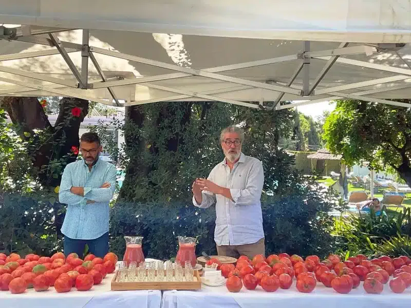 Dos hombres promocionando los beneficios para el bienestar de una mesa llena de tomates.