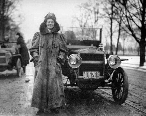 A woman in a coat showing well-being next to a car.
