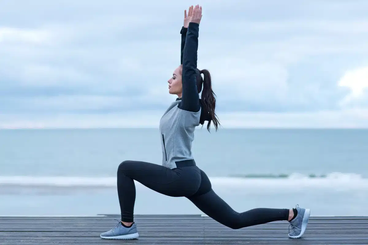 A woman doing squats in front of the ocean to promote wellness and fitness.